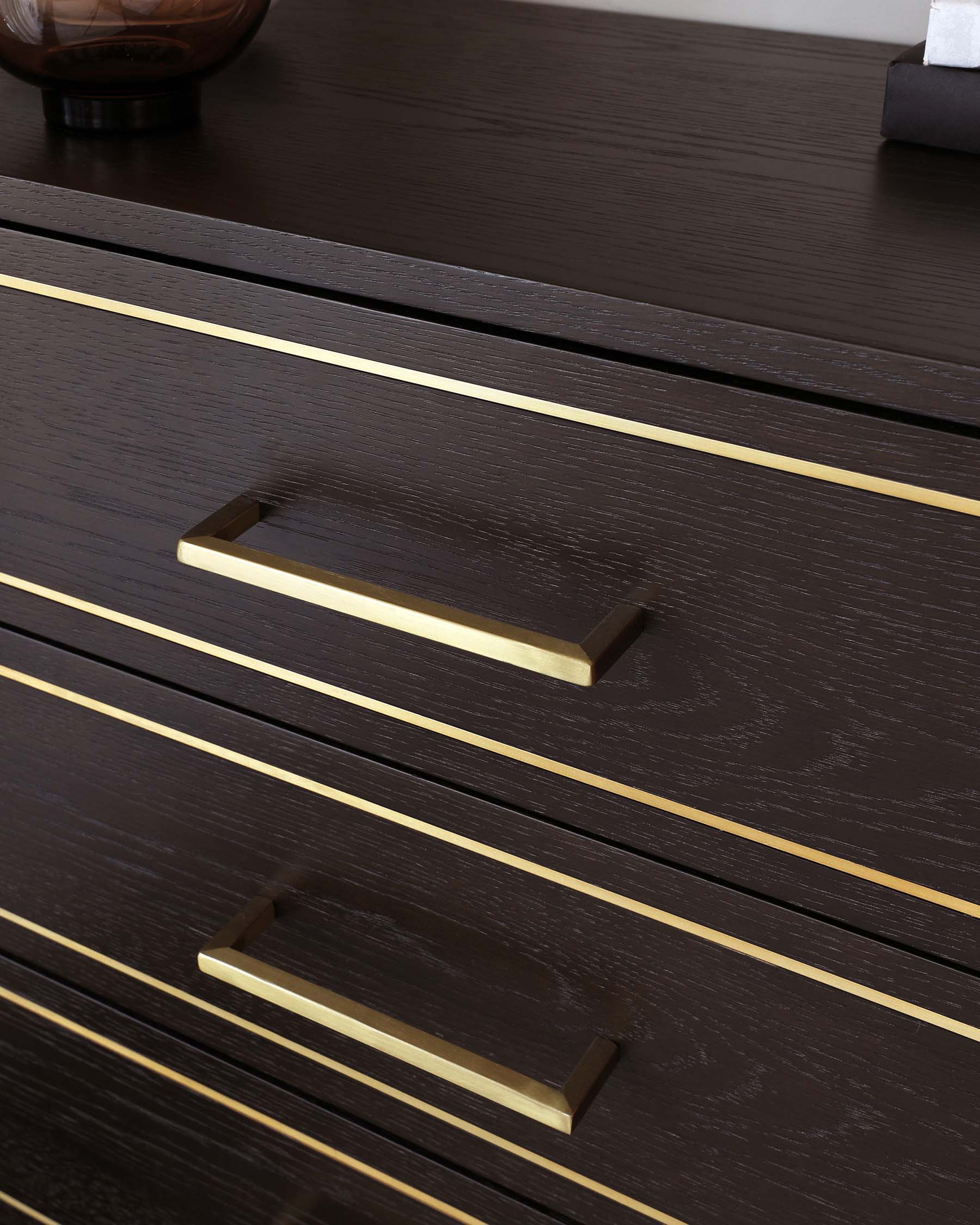 Modern dark wooden furniture with sleek brass handles on drawers featuring elegant, slimline brass inlays for a contemporary design aesthetic.