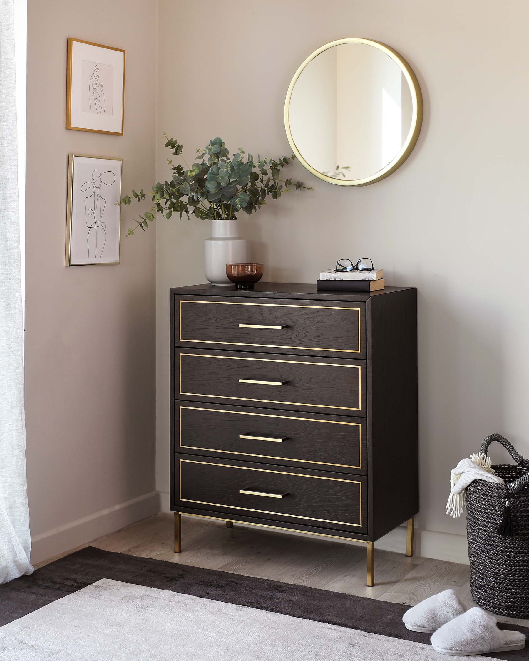 Modern, dark-toned wooden chest of drawers with four drawers embellished with sleek brass handles and matching brass legs. A circular, brass-framed mirror is hanging on the wall above it.