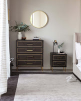 Elegant bedroom furniture set with a dark wood finish and gold metal accents. The collection includes a tall five-drawer dresser and a two-drawer nightstand, both featuring sleek handles and raised on tapered legs. A simple, yet sophisticated design ideal for a modern home interior.