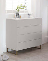 Modern white four-drawer dresser with a minimalist design and elegant brass-finished metal legs.