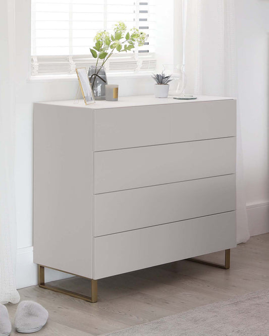 Modern white four-drawer dresser with a minimalist design and elegant brass-finished metal legs.