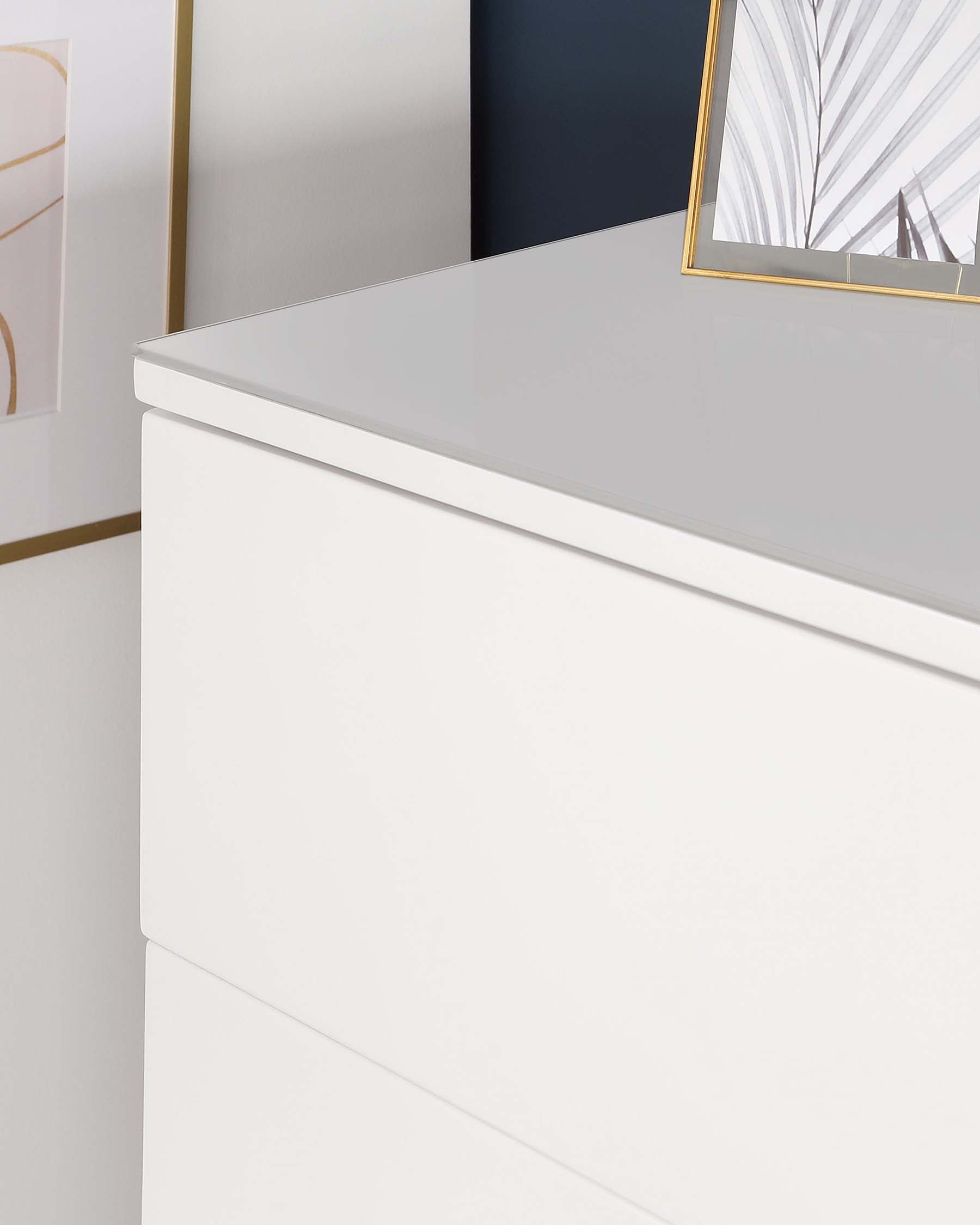 Modern white high-gloss dresser with sleek handles and a minimalist design, partially visible, adorned with a framed abstract artwork leaning against the wall.