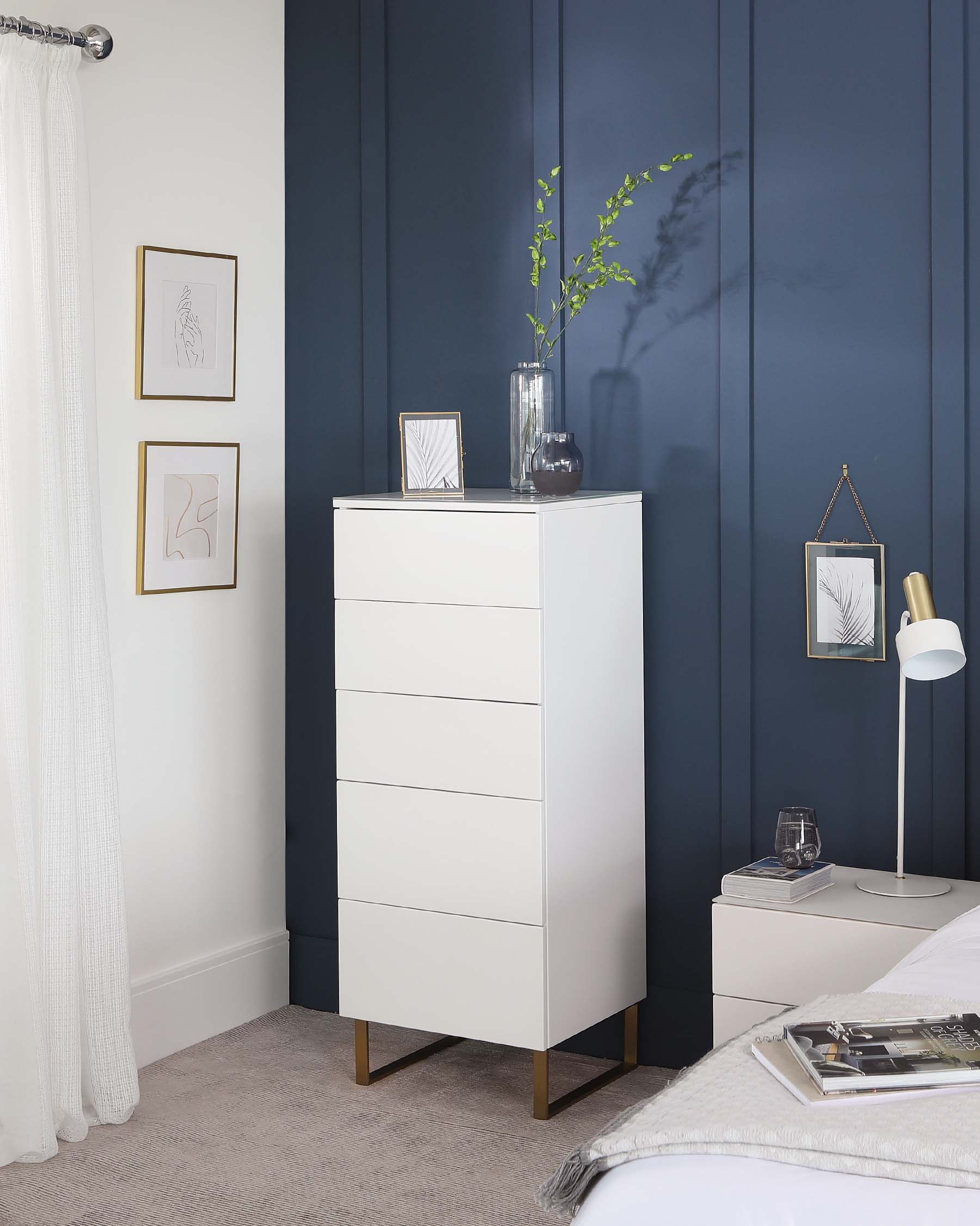 Modern white tallboy dresser with five drawers, featuring sleek handles and tapered wooden legs in a bedroom setting.