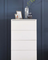 A modern white four-drawer chest against a dark blue wall.