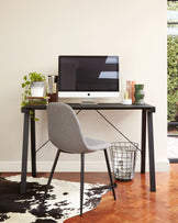 Modern minimalist home office setup featuring a sleek black desk with straight legs and a grey fabric upholstered chair with slender black metal legs. A wire trash can is positioned beside the desk.