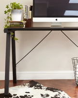 Modern minimalist black desk with a sleek surface and angled legs, complemented by an angular metal support beam.