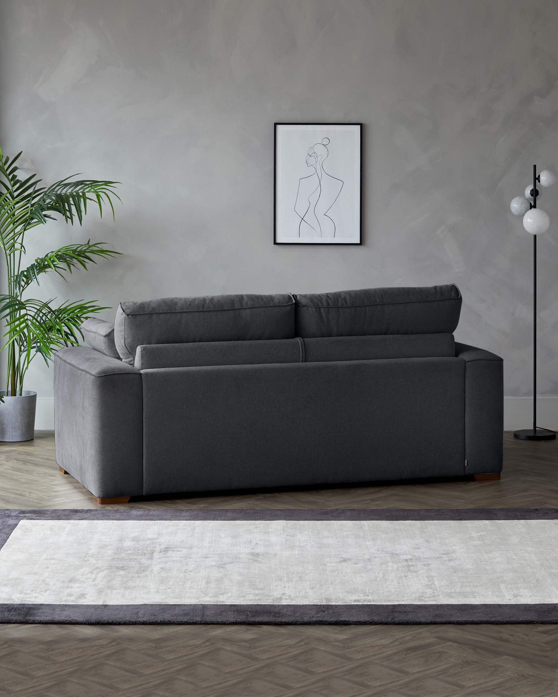 Contemporary charcoal grey fabric sofa with plush cushions and clean lines, sitting on wooden legs, paired with a contrasting two-toned modern area rug in shades of grey and cream.