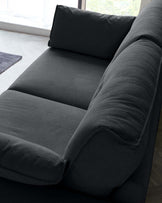 Modern charcoal grey sofa with a streamlined design, featuring plush back cushions, a deep fixed seat, and a full-width side armrest cushion. The sofa is upholstered in a textured fabric, adding a touch of sophistication to the sleek silhouette.