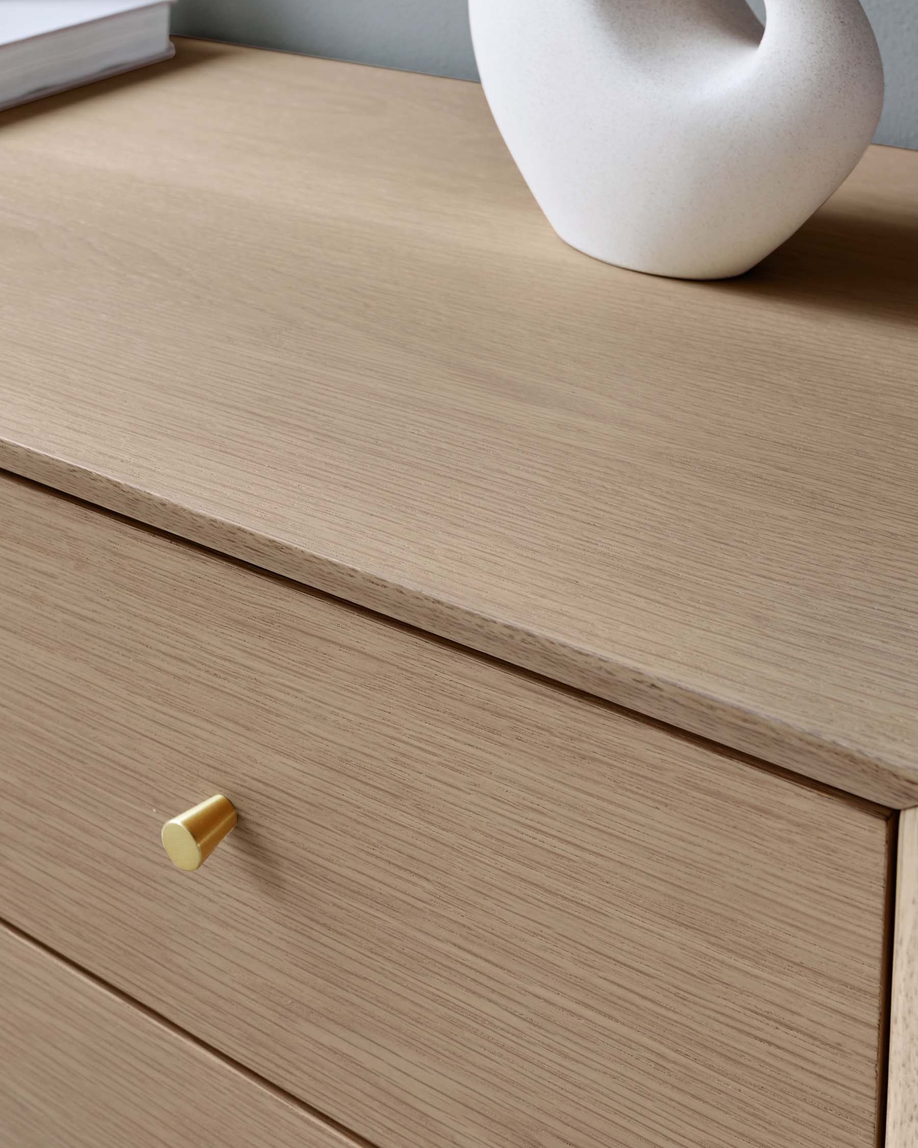 Light-coloured wooden drawer unit with a minimalist design, featuring a smooth finish and a cylindrical, golden knob on the drawer front.