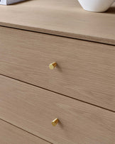 Modern light wood finish drawer chest with cylindrical gold-tone handles.