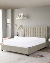 Modern upholstered bed with a tufted headboard in a neutral beige fabric, accompanied by a minimalist white bedside table with sleek lines to the right.