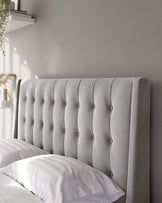 Elegant tufted headboard in a light grey fabric with a vertical channel design and button details, providing a luxurious and comfortable backrest for a bed.