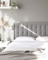 Elegant upholstered grey headboard with tufted buttons and a sleek white nightstand with a modern white lamp.