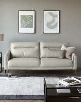 Modern light grey three-seater sofa with clean lines and plush cushions, accented with a mix of solid and patterned throw pillows. In front, a low-profile espresso-hued coffee table with glass top and sleek straight legs, resting on a subtle grey ombré area rug.