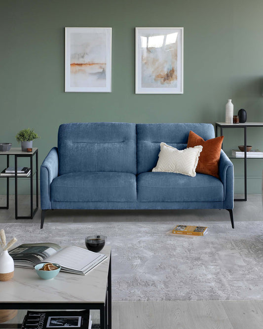 A blue sofa with decorative pillows, two side tables, a coffee table with magazines, and artwork on the green wall.