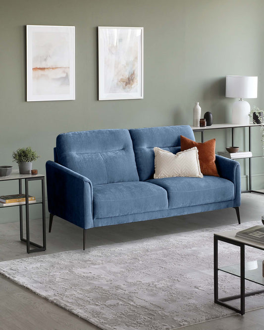 A plush blue sofa with decorative pillows, accompanied by black side tables, a light lamp, and stylish wall art in a cozy setting.