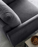 A contemporary dark grey fabric sofa with plush cushions and clean, straight lines on a light wooden floor, with a small white side table and a bowl of dried citrus slices on it.