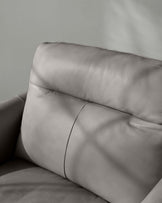 Close-up of a modern grey leather sofa highlighting the texture and stitching details on the upholstery.