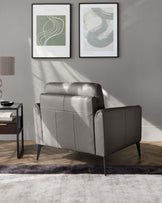 A modern grey leather loveseat with a clean, linear design and metal legs, accompanied by a sleek, dark-framed side table with an open shelf and drawer, all atop a two-tone grey area rug in a contemporary living space.