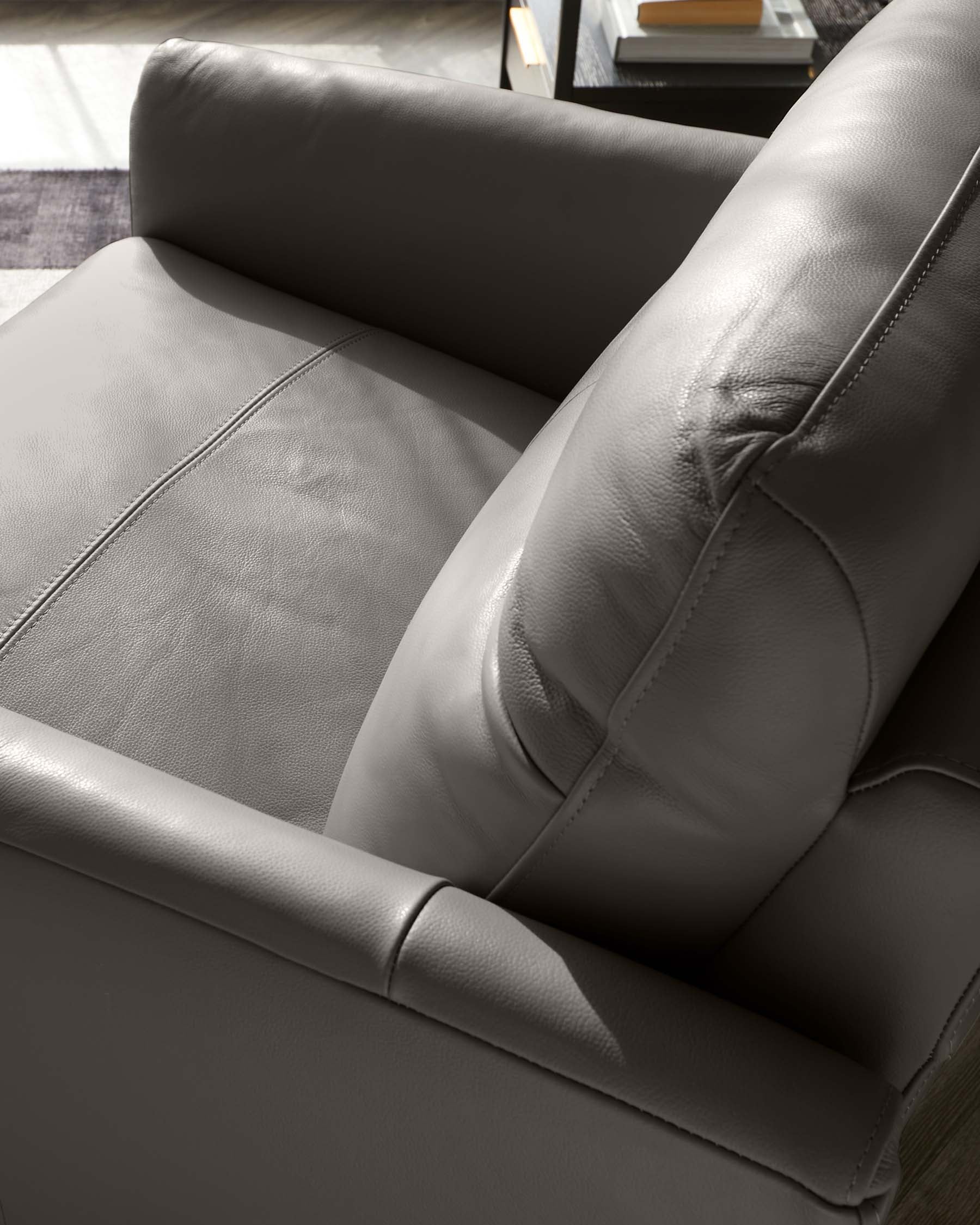 Close-up view of a modern leather armchair in grey, with visible stitching detail, a plush seat, and padded armrests.