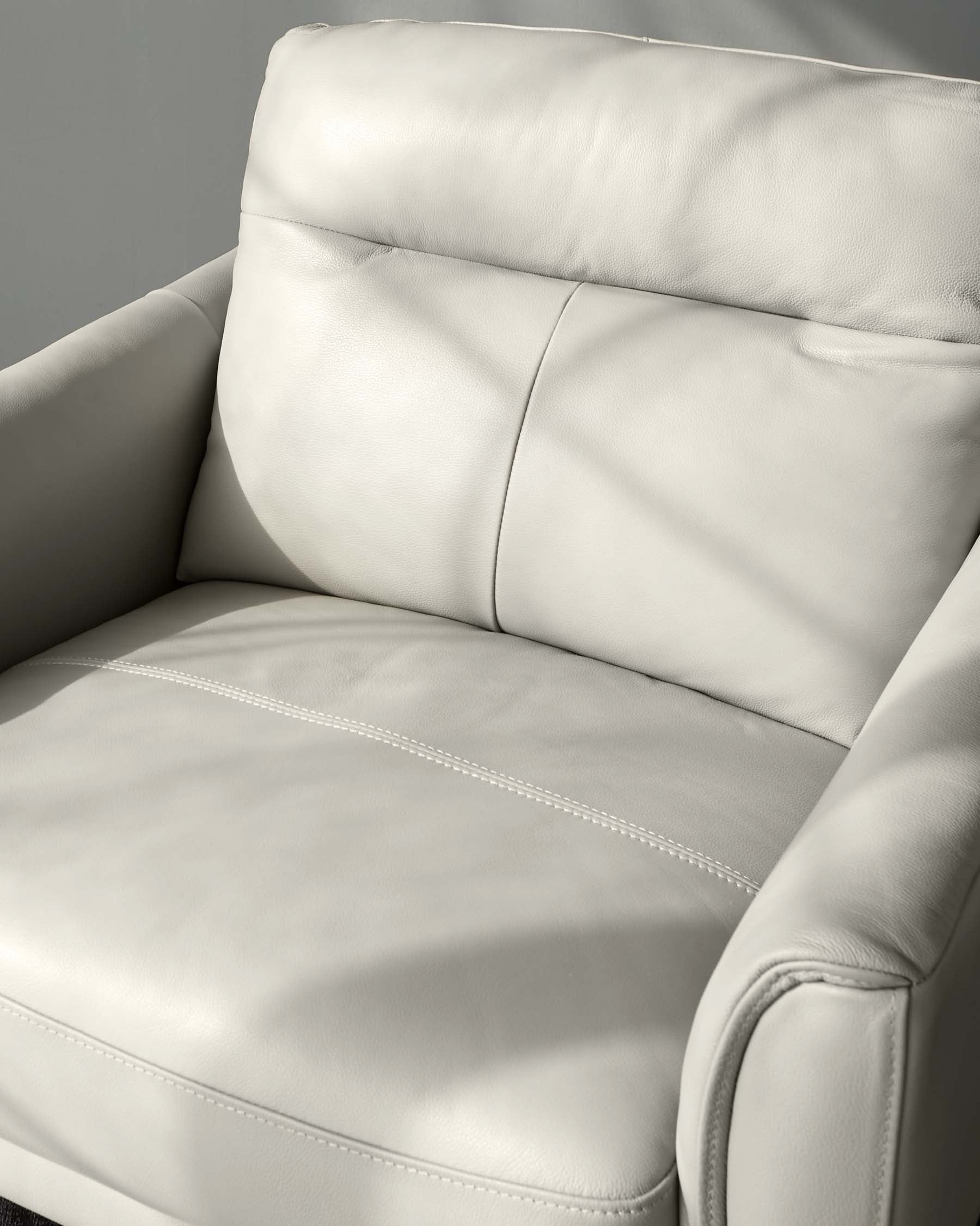 Close-up of a contemporary style cream-colored leather armchair showcasing plush cushioning, detailed stitching, and a high backrest.