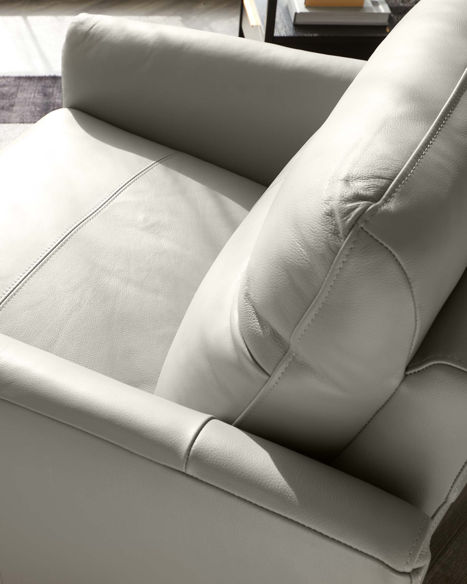 Close-up of a modern light beige leather armchair with plush cushions and fine stitch detailing.