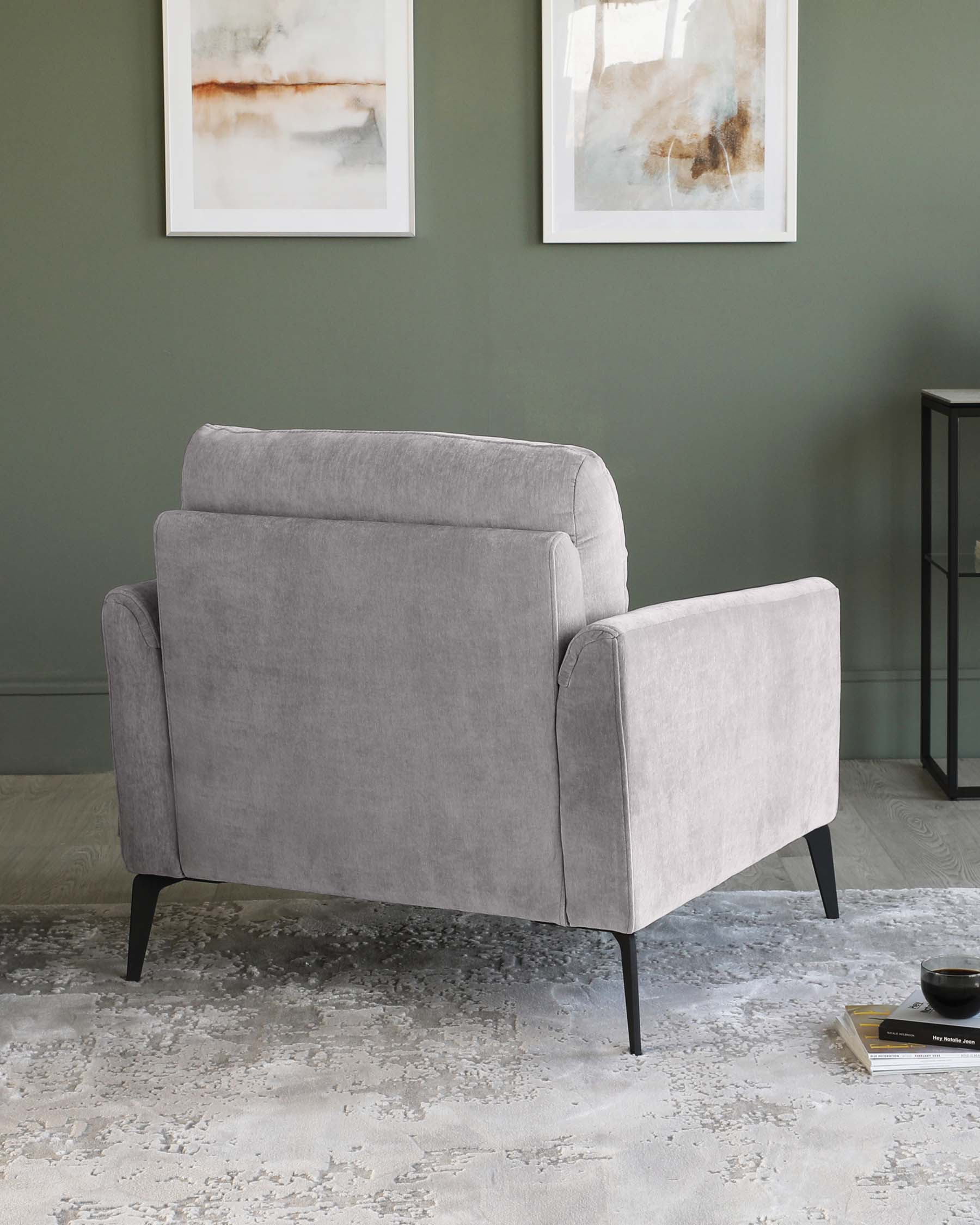 Modern light grey armchair with clean lines and black metal legs, positioned on an abstract-patterned off-white area rug, with minimalist framed artwork on a green wall in the background and a small black side table to the right.