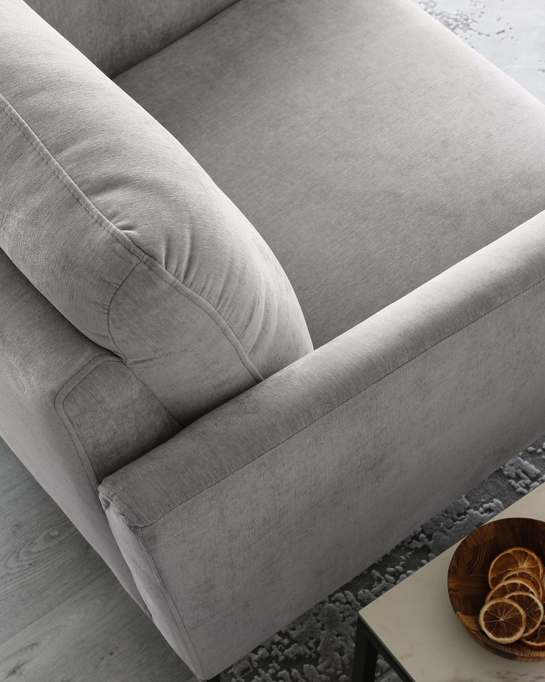 Modern light grey fabric sofa with clean lines, featuring plush back cushions and a deep, comfortable seat. The couch rests on a minimalistic, hidden base, complemented by a small wooden bowl with dried citrus slices on the adjacent side table.