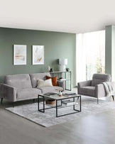 Modern living room featuring a grey three-seater sofa with plush cushions and matching armchair, a square black metal coffee table with a glass top and lower shelf, and a tall, narrow side table with a black frame and glass shelves. The area is accented with a textured grey rug and off-white curtains, creating a sleek, contemporary space.