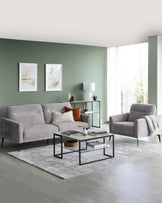 Modern living room set featuring a three-seater sofa and matching armchair in light grey fabric upholstery with sleek black metal legs. In front of the sofa is a rectangular metal and wood coffee table with a lower shelf, accompanied by a smaller round side table with a similar design. A green console table with shelves stands against the wall, complementing the room's muted colour palette. The furniture rests atop a textured grey area rug, creating a cohesive contemporary look.