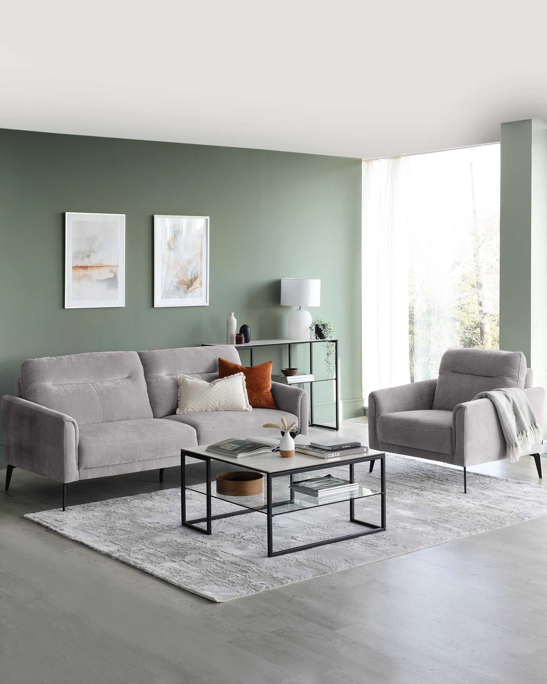 Contemporary living room featuring a grey fabric upholstered sofa and a matching armchair, complemented by a set of black metal frame nesting coffee tables with a glass top and a wooden round detail. A coordinating side table with a glass shelf displays decor items. The seating is adorned with assorted throw pillows, and the arrangement is grounded by a light grey textured area rug.