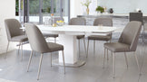 Modern dining room furniture set featuring a white oval table with a sleek pedestal base and six taupe upholstered chairs with slender metal legs.