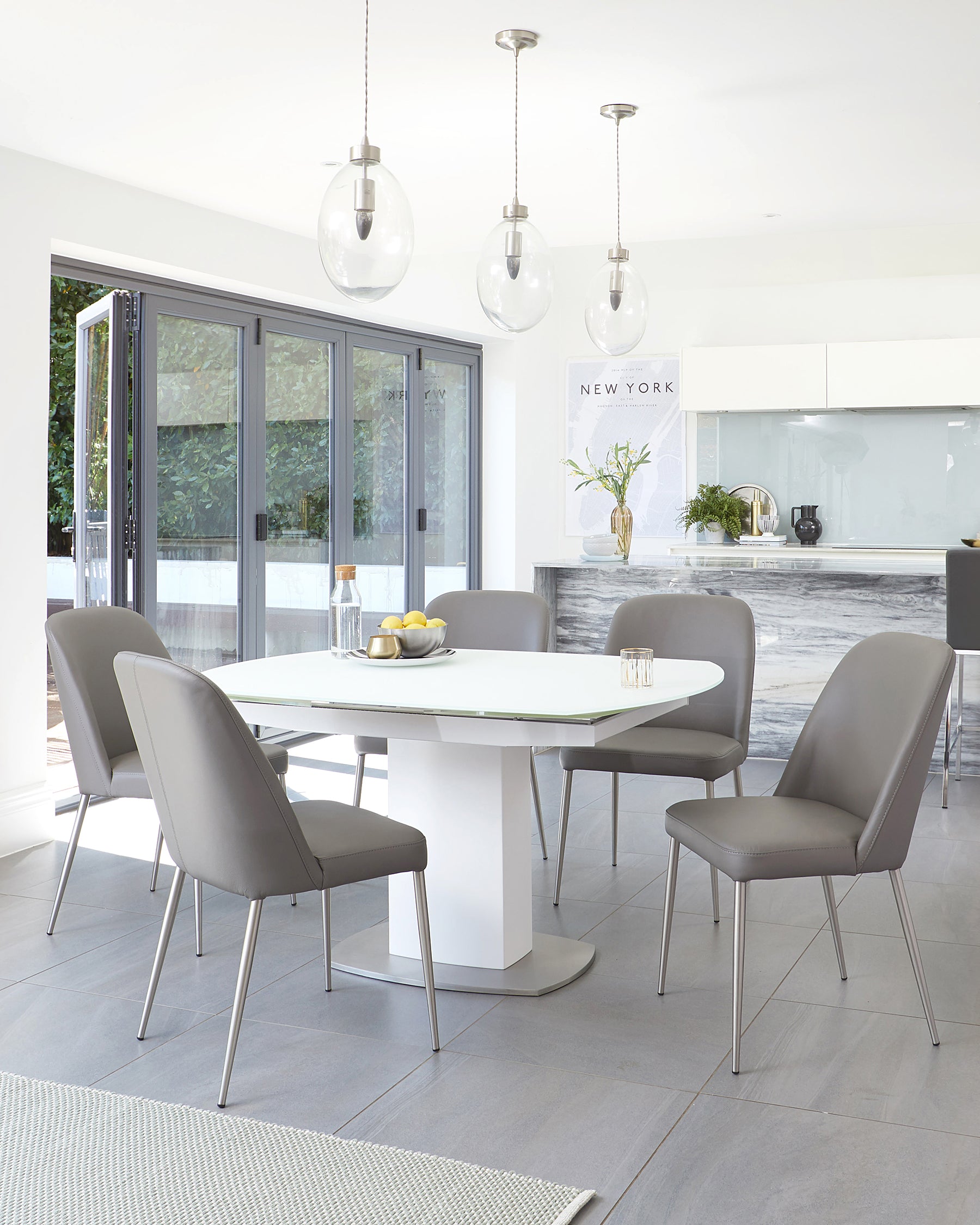 Modern dining room furniture featuring a white rectangular table with a sleek, pedestal base and six taupe upholstered chairs with slim metal legs.