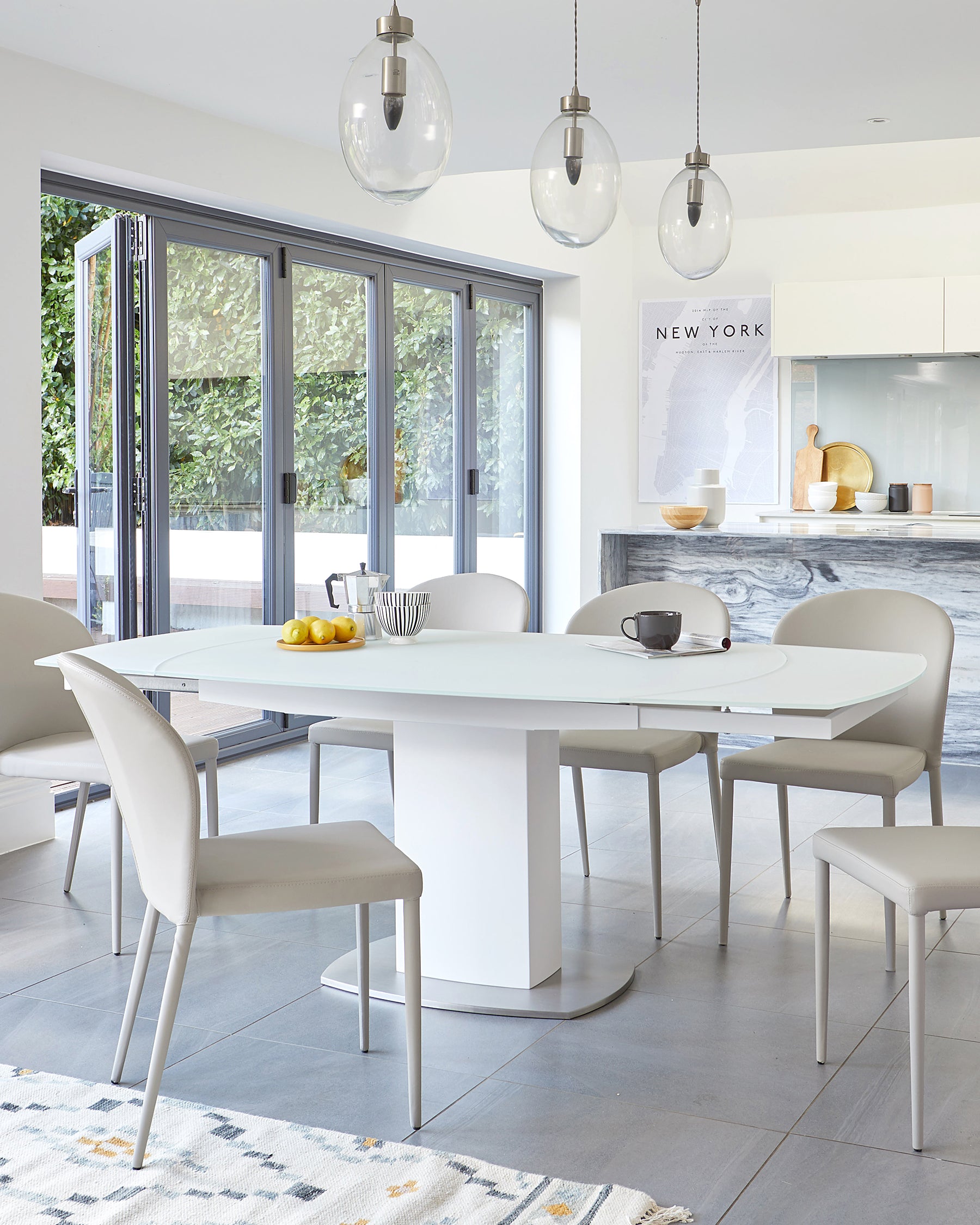 Modern dining room with an oval white table and sleek, metallic base, surrounded by matching white upholstered chairs with metal legs.