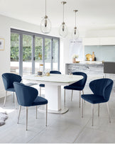 Modern dining set featuring a white oval table with a central pedestal base and four navy blue upholstered chairs with sleek metal legs.