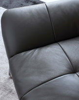 Close-up of a modern luxury dark grey leather sofa with textured upholstery and sleek design, partially shown against a grey carpeted floor.