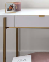 A modern minimalist white console table with a thin sleek rectangular tabletop and a single drawer with a brass knob handle. The table is supported by a slim, geometric frame consisting of vertical brass legs connected to the tabletop and a horizontal brass bar at the base.