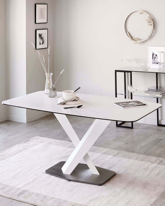 Modern minimalist dining table with a white rectangular top and a distinctive X-shaped metallic base, along with a sleek black console table featuring a glass top and slender metal frame, placed against a neutral-toned room with decorative wall art and a subtle area rug.