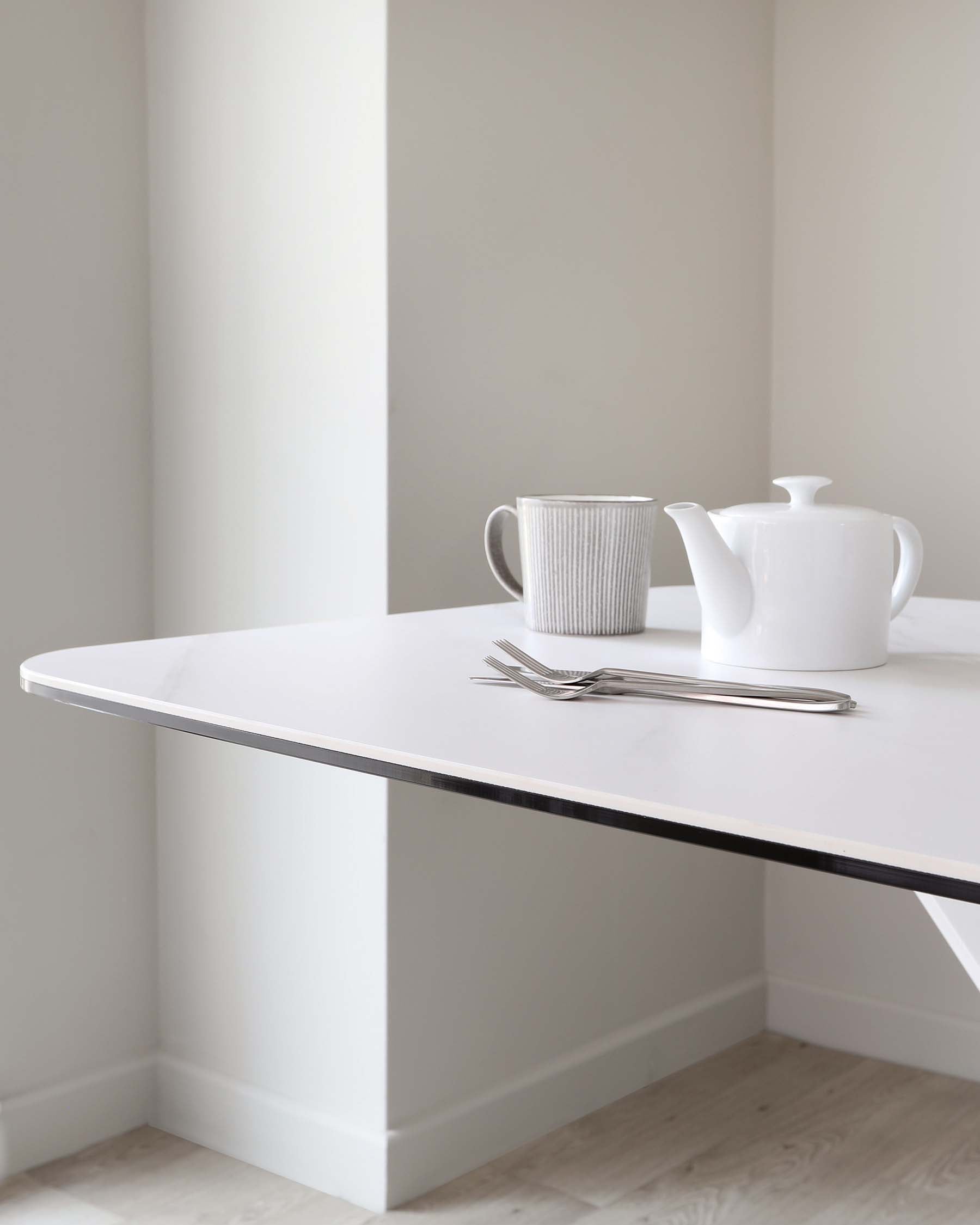 A minimalist white dining table with a sleek, modern design, featuring a smooth, rectangular tabletop with rounded corners and a single, sturdy base that supports one side of the table, creating an elegant floating table edge effect. The base has a clean, flushed look with the wall, suggesting a built-in or custom installation.