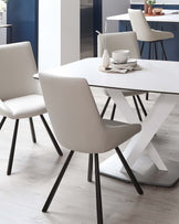 Modern dining set featuring a white marble-top table with a unique X-shaped metallic base, accompanied by stylish cream upholstered chairs with sleek black legs.