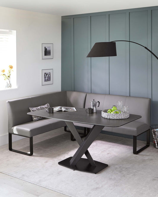 Contemporary dining set featuring a sleek, dark grey corner bench with a smooth faux leather finish, paired with a matching modern dining table with a unique X-shaped metallic base.