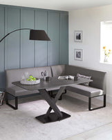 A modern dining set featuring a rectangular table with matte black finish and a distinctive X-shaped leg base. Accompanied by an L-shaped, grey upholstered bench with clean lines and simple design, all situated on a light grey area rug.