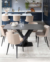 Modern rectangular dining table with a dark grey top supported by a bold black X-shaped base, surrounded by six beige upholstered chairs with black tapered legs, set on a faded off-white area rug.