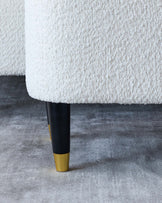 Close-up of a modern furniture leg with a bouclé fabric upholstery and a tapered design, featuring a black finish with a gold metallic accent on the foot.