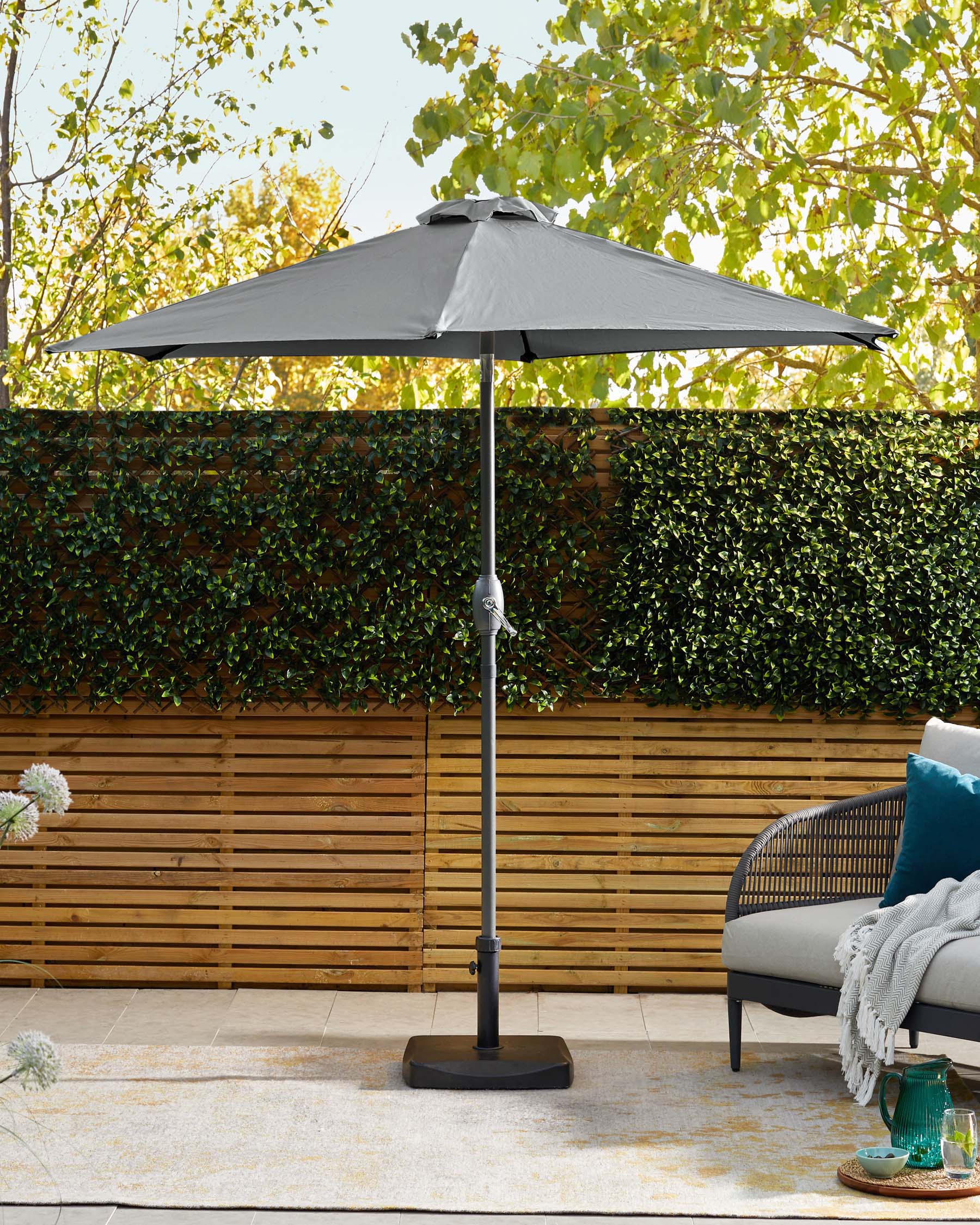 A stylish outdoor patio umbrella in gray, featuring a sturdy base and surrounded by greenery, alongside a modern seating area.