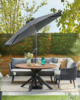 A stylish outdoor seating area featuring a round table, a modern sofa with cushions, and a large umbrella for shade.