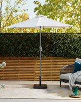 A stylish outdoor umbrella with a white canopy, supported by a sturdy base, alongside a modern woven patio sofa with cushions.