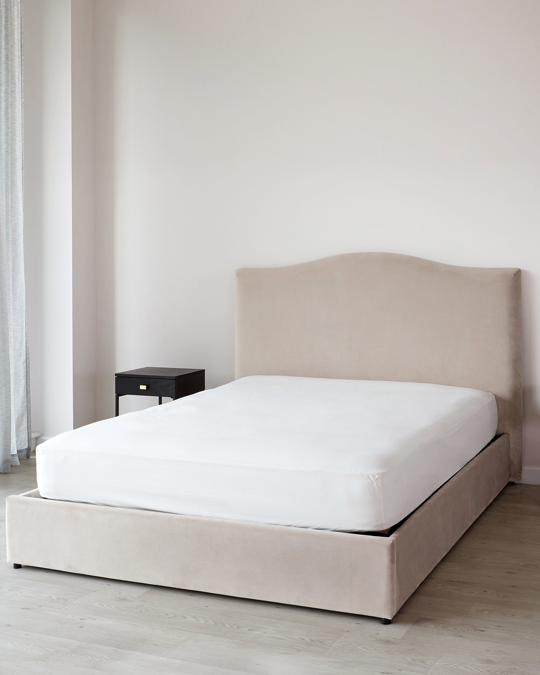 Elegant contemporary bedroom furniture featuring a beige upholstered bed frame with a curved headboard, a white mattress, and a simple black bedside table.