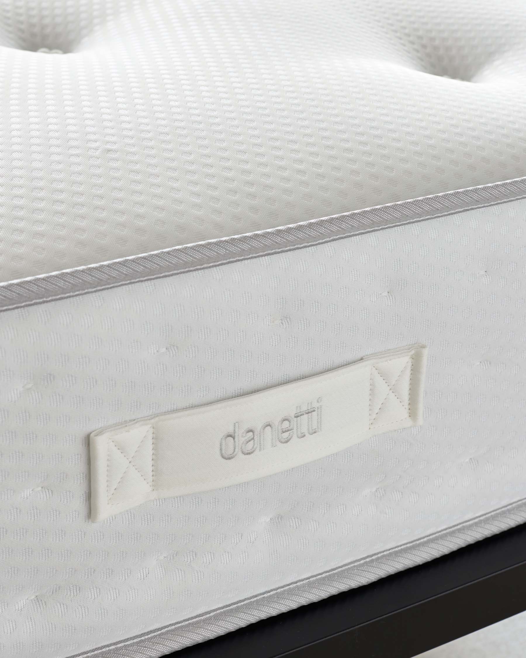 Close-up of a textured white mattress with a detailed edge stitching and a branded label that reads "Danetti."