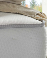 Elegant close-up of a textured fabric ottoman in neutral tones with a beige knit throw blanket neatly draped over one corner, suggesting a cosy and stylish interior aesthetic.